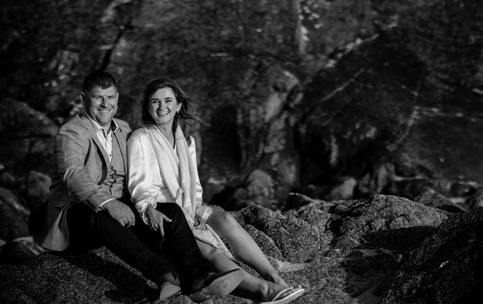 the newlywed couple sit on the rocks at St Ouens bay after their elopement wedding in St Helier, Jersey, CI