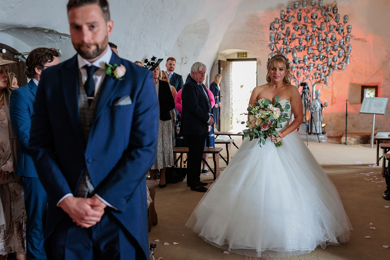 The bride walks down the aisle to meet her future husband at Mont Orgueil Castle, Jersey. The groom looks nervous