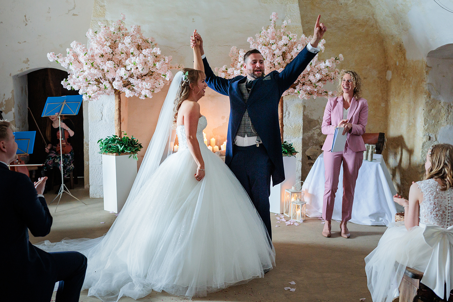 The groom throws his arms up in the air triumphantly as he and his bride become legally married at Mont Orgueil Castle, Jersey